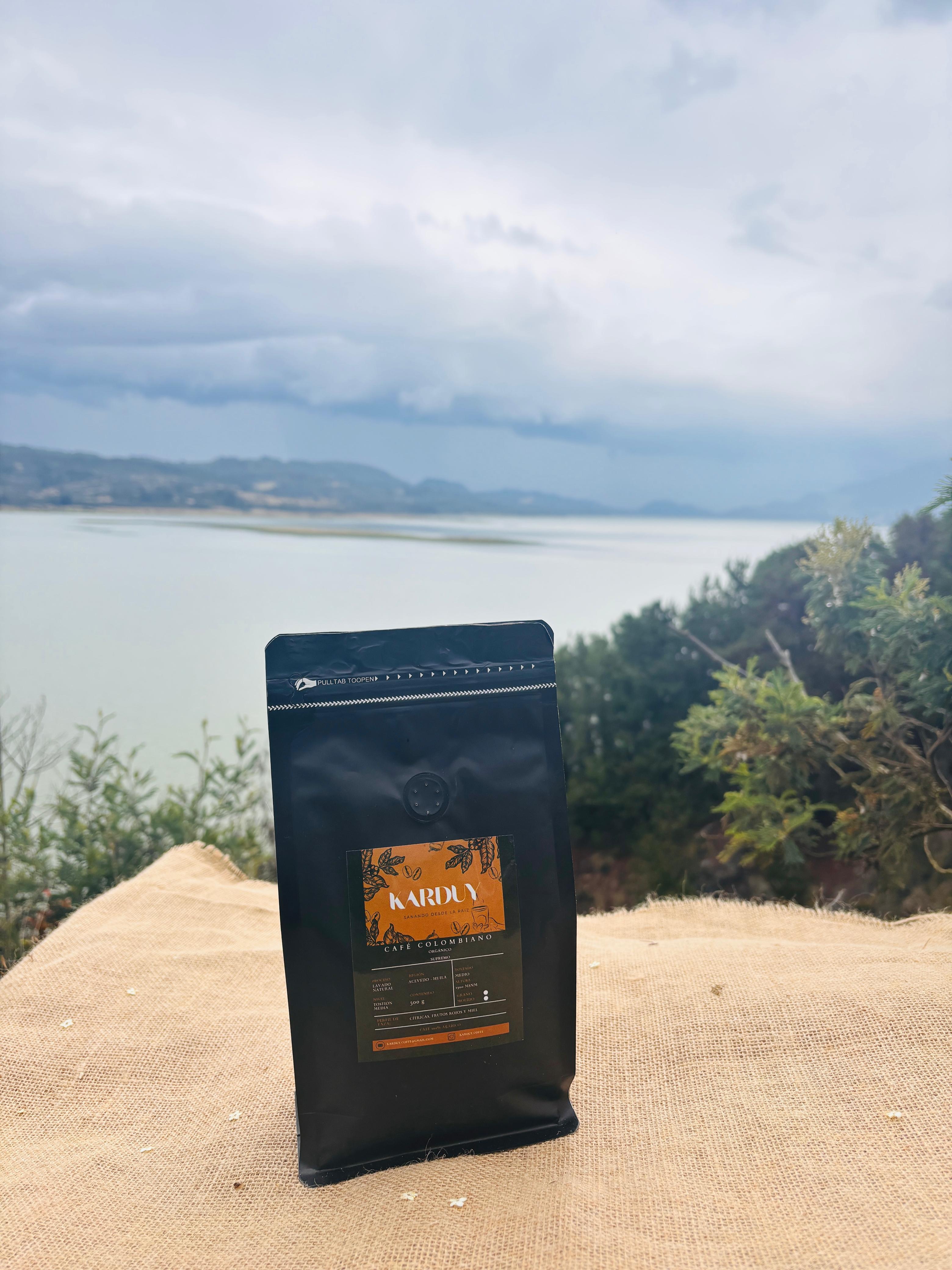 Bolsa de Café 100% Colombiano Karduy sobre mesa de fique con el embalse de Guatavita al fondo