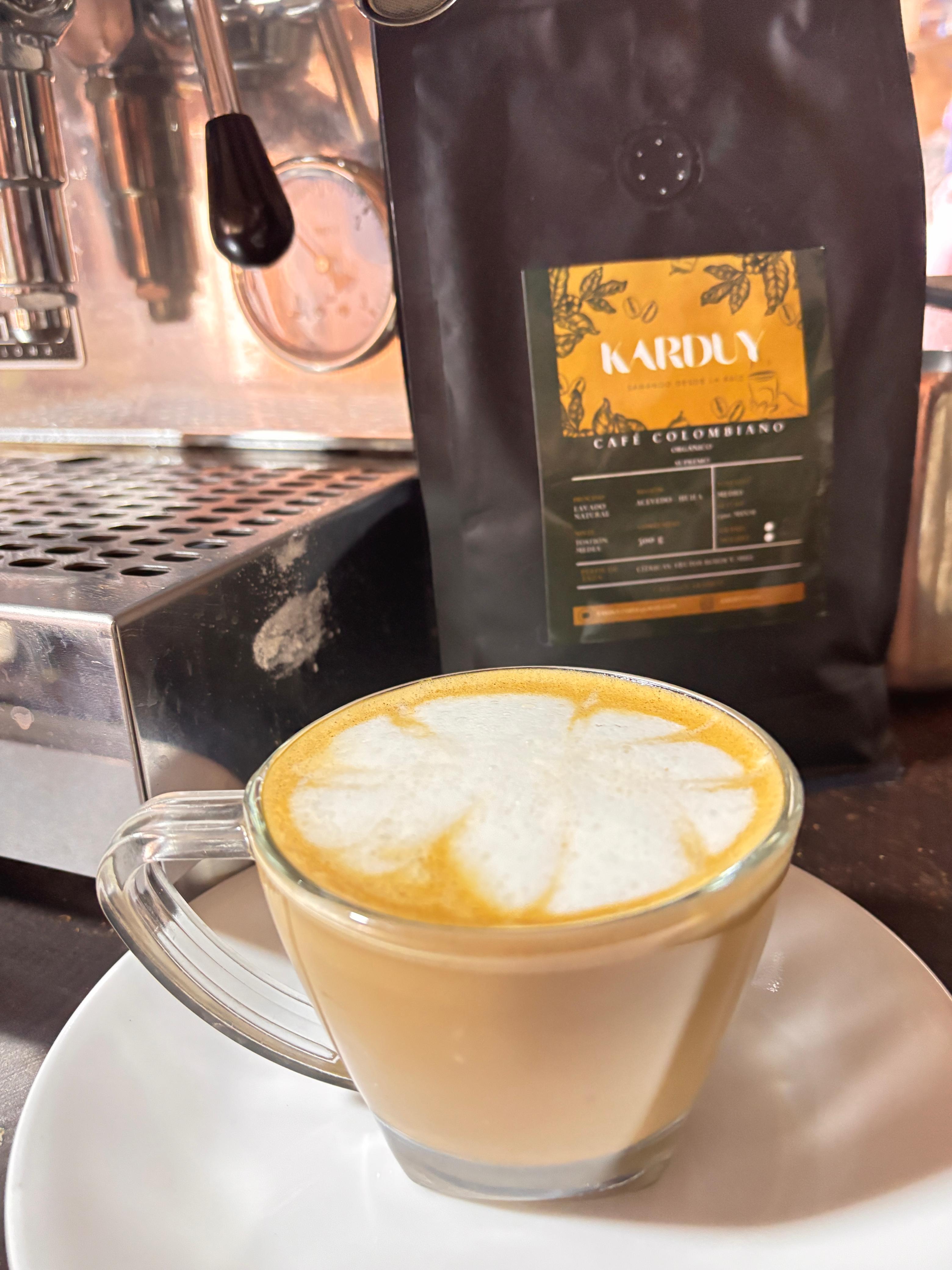 Café con leche preparado con granos de Café 100% Colombiano Karduy, junto a la bolsa del producto